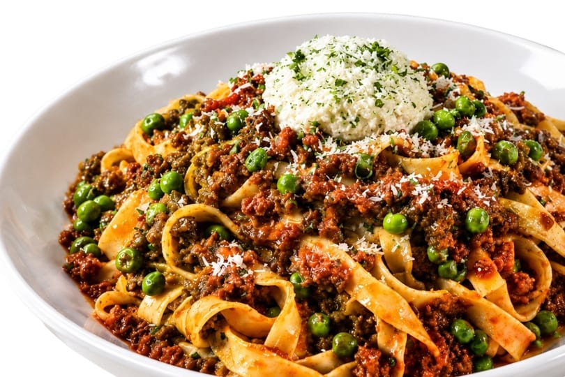Close-up of pasta with meat sauce, green peas, and a dollop of ricotta cheese.