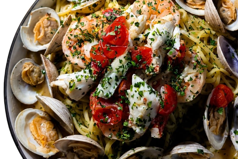 Close-up of seafood pasta with clams, shrimp, crab, cherry tomatoes, and parsley.